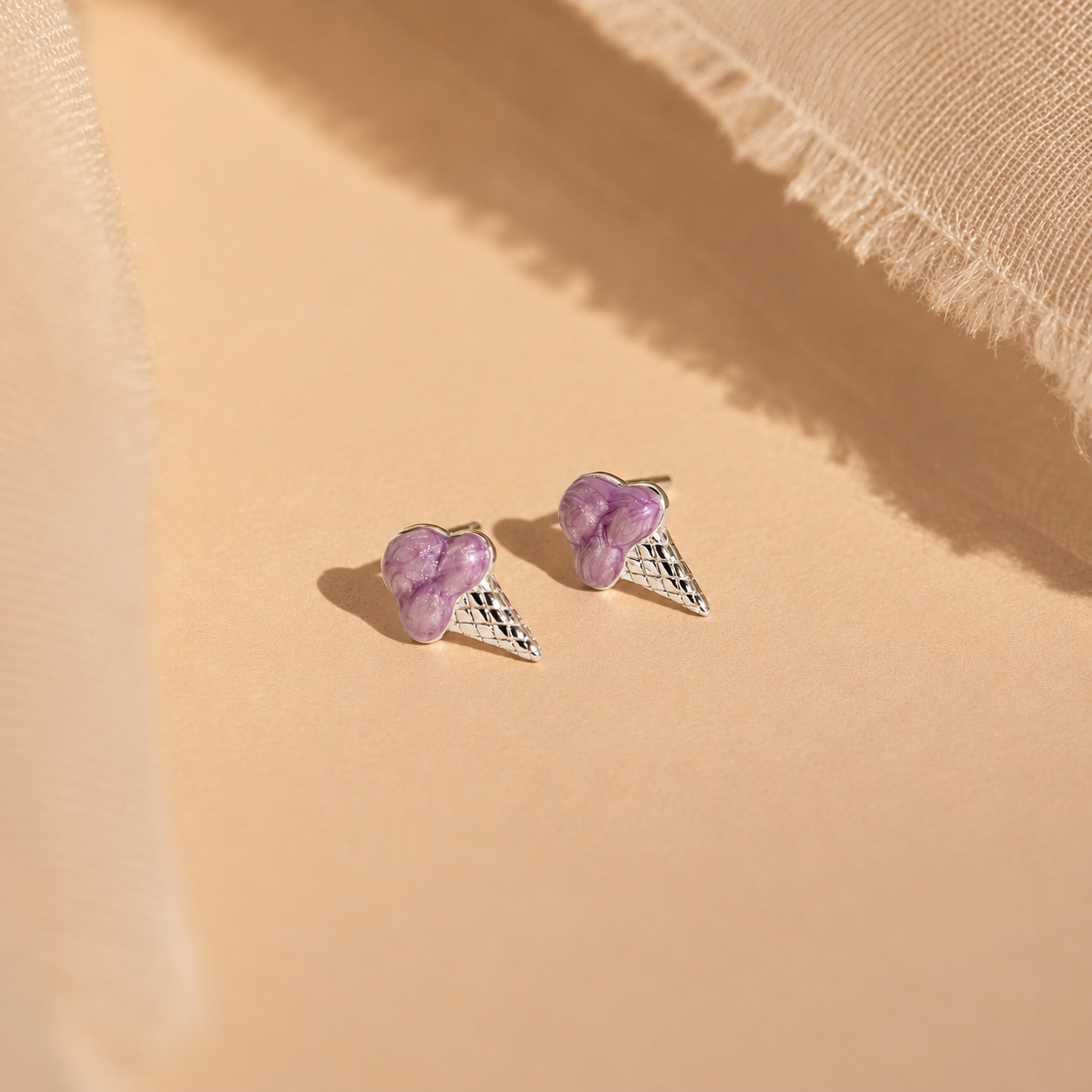 Pair of purple heart-shaped earrings with silver wings on a beige fabric background